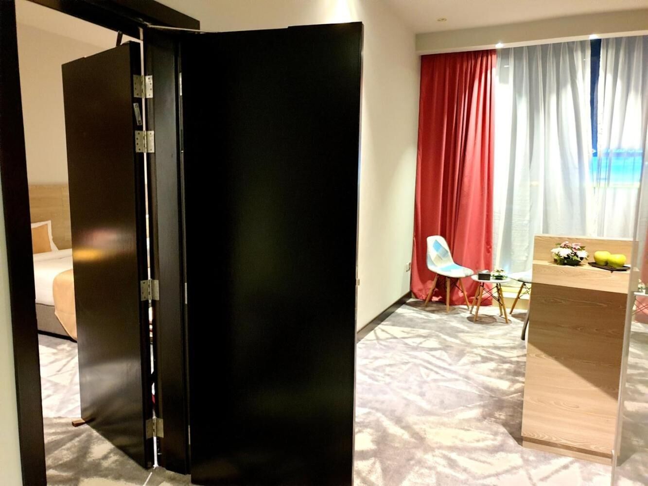 Hotelkamer met een bed, bureau, stoel en groot raam met rode gordijnen.
