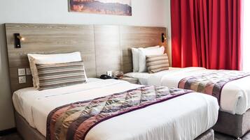 A hotel room with two beds, each with a wooden headboard, white bedding, and striped pillows. There is a painting on the wall and a red curtain on the window.
