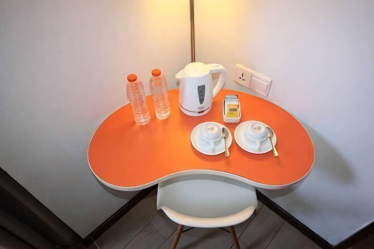 Una mesa pequeña con un hervidor blanco, dos tazas, un plato y dos botellas.