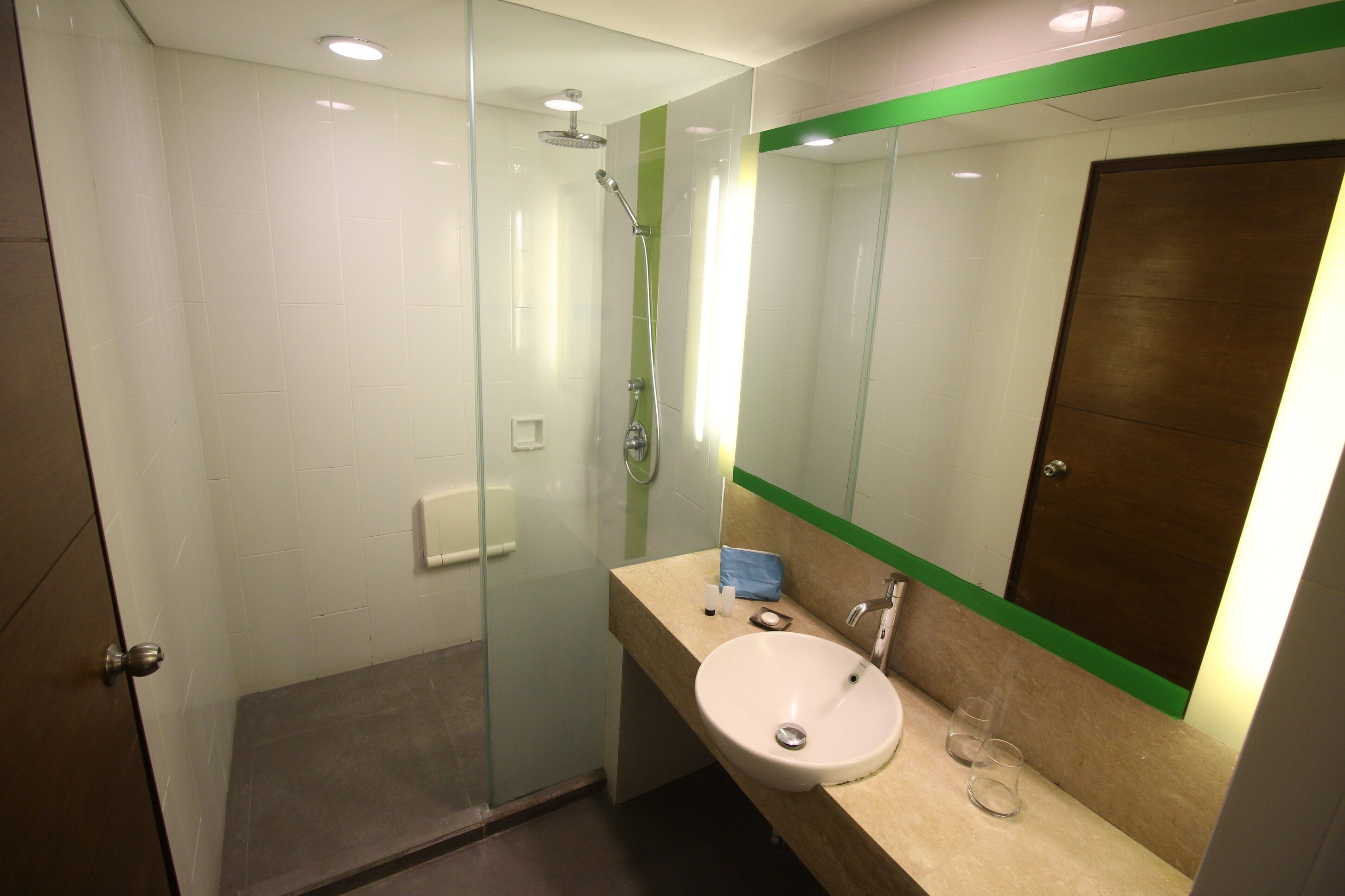 A modern bathroom with a glass shower enclosure, a sink with a mirror, and a wooden door.