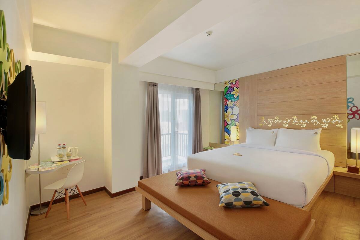 Habitación de hotel con cama, escritorio, silla, televisor y ventana con cortinas.