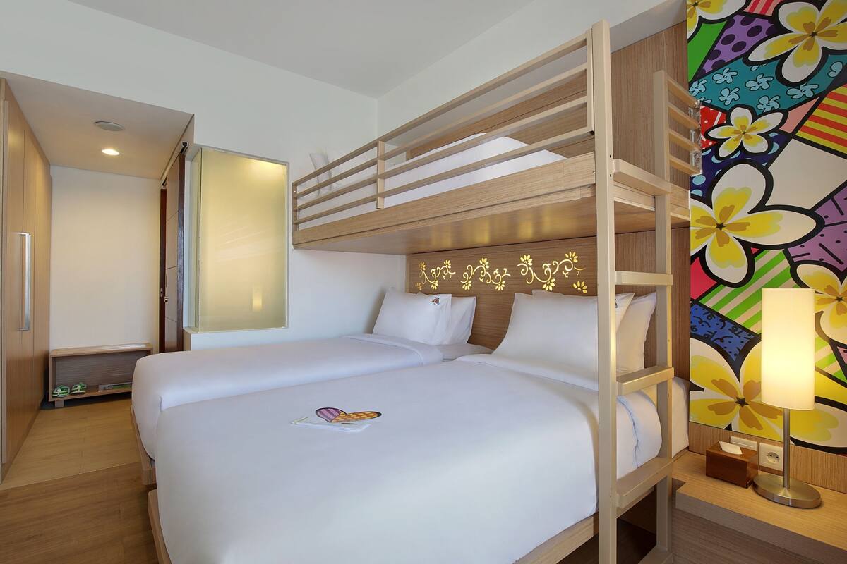 Habitación de hotel con literas, una mesita de noche con lámpara y un llamativo mural floral.
