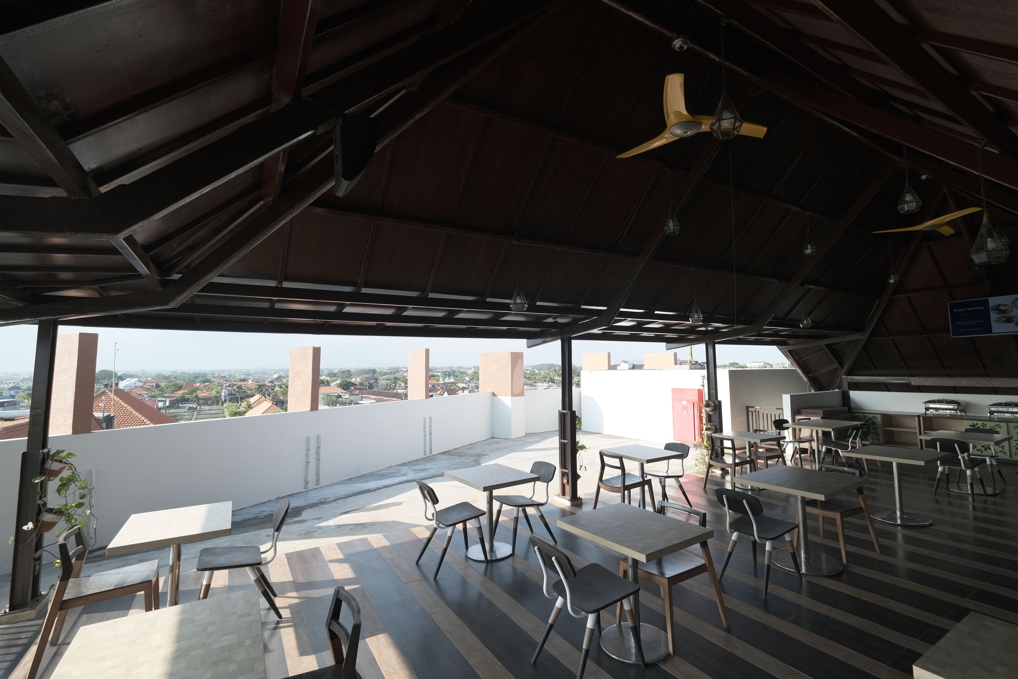 An outdoor dining area with tables and chairs, a ceiling fan, and a view of the cityscape.