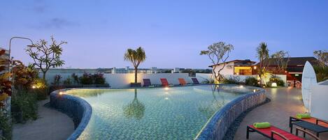 Una piscina con borde de azulejos, sillas de descanso y una palmera.
