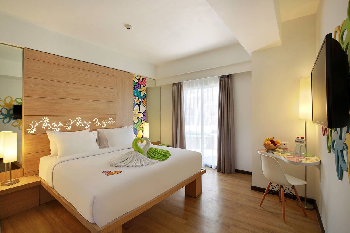 Habitación de hotel con una cama grande, un escritorio con silla, televisión y ventana con cortinas.