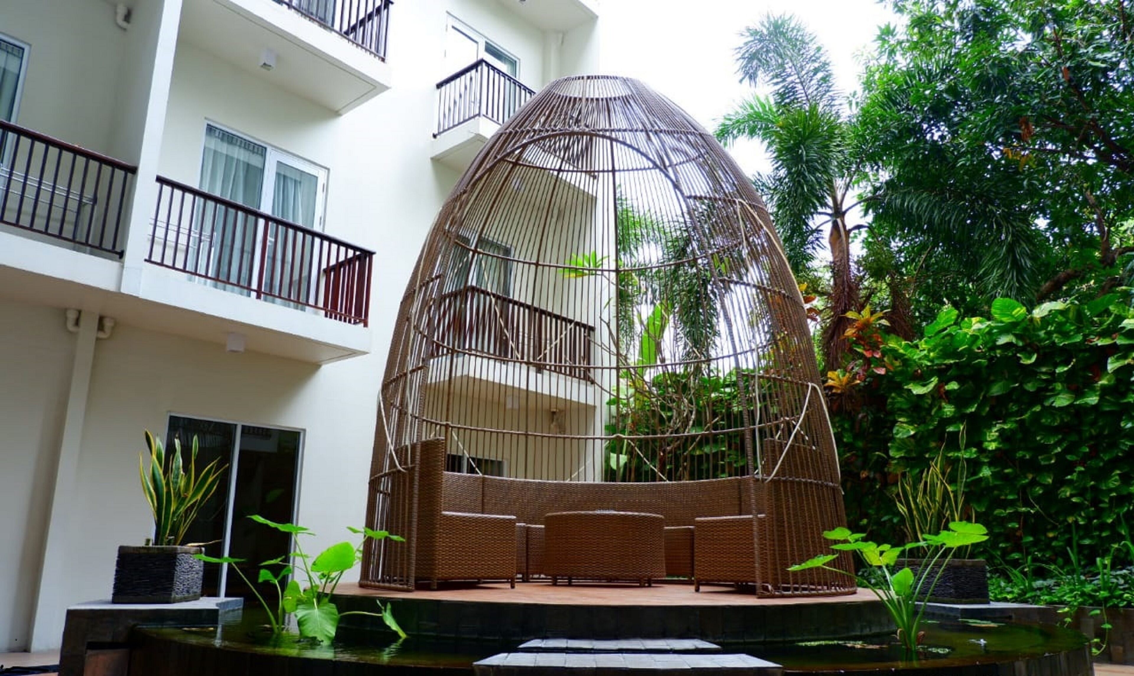 A modern building with a balcony, a hanging chair, and a small garden area with plants and a water feature.