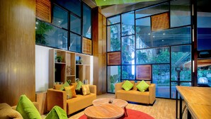 A modern living room with two sofas, a coffee table, and a bookshelf. Large windows provide a view of the outside. - Nikhila Seminyak (Keroboken Kelod)