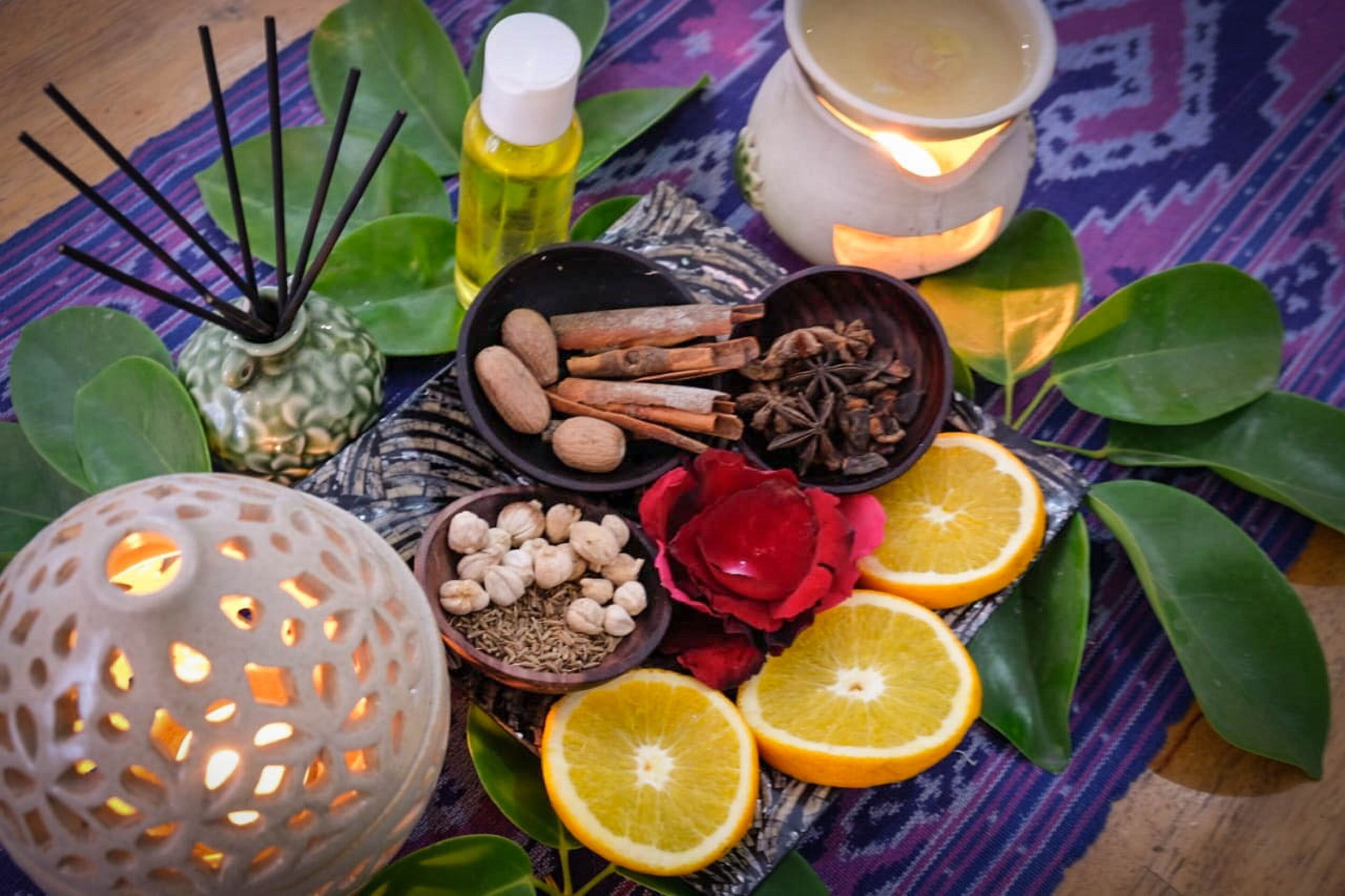 A table with a decorative candle, a bowl of spices, a flower, and citrus slices.