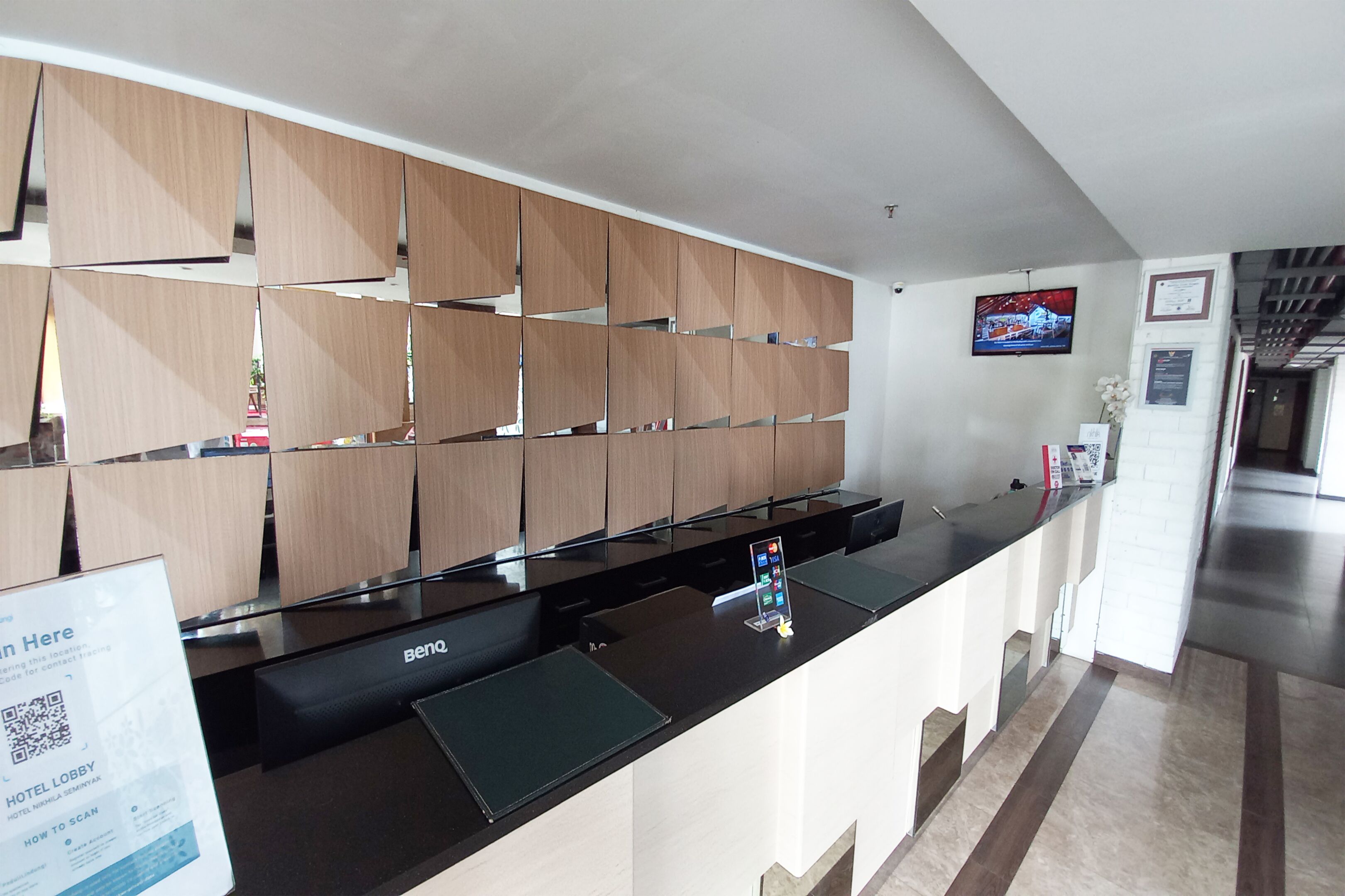 Un hall de hotel con mostrador de recepción, pared de paneles de madera, una pantalla de televisión y un letrero con un código QR.