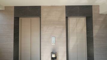 A modern elevator with a metallic finish, flanked by dark marble panels and a light wood panel.