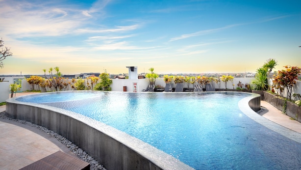 A rooftop infinity pool with a clear view of the city skyline, surrounded by potted plants and a small white structure. - Nikhila Seminyak (Keroboken Kelod)