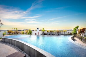 A rooftop infinity pool with a clear view of the city skyline, surrounded by potted plants and a small white structure. - Nikhila Seminyak (Keroboken Kelod)