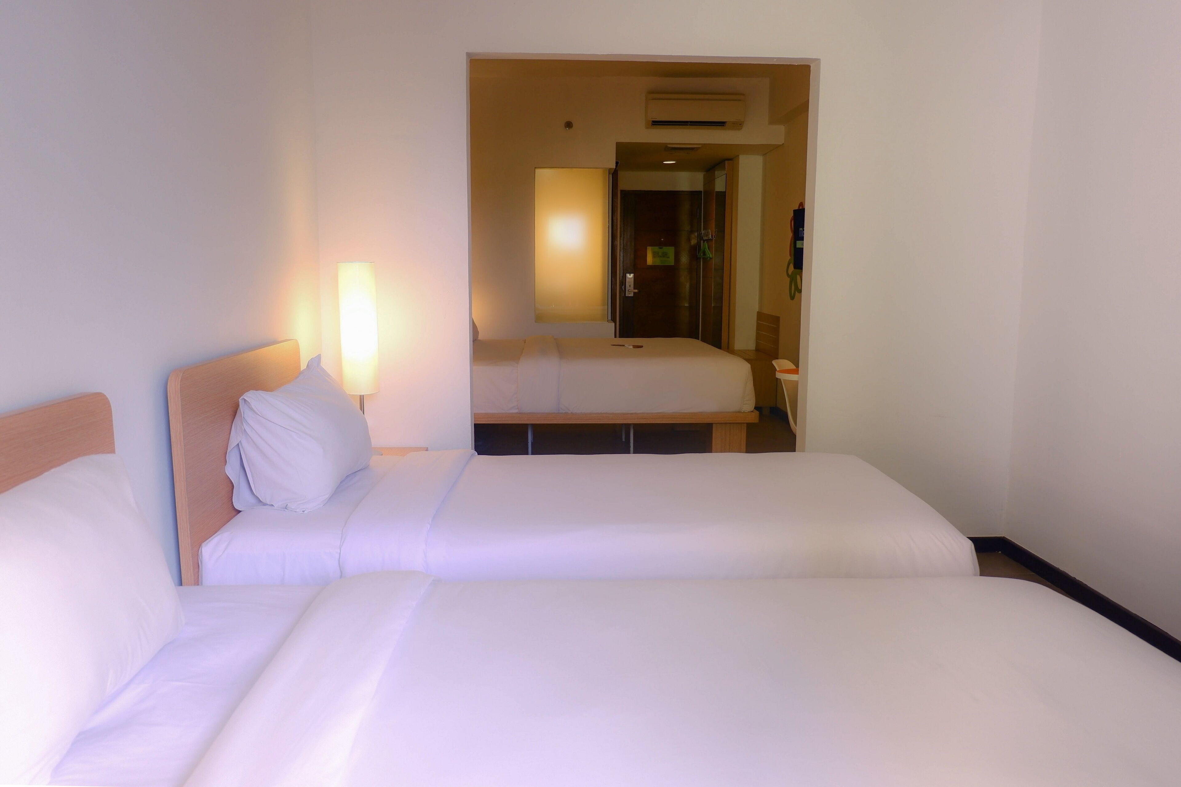 Habitación de hotel con dos camas, una mesita de noche, una lámpara y una puerta que da a un baño.