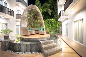 Un espacio de estar circular al aire libre con estructura tejida, rodeado de escalones de piedra y una fuente de agua.