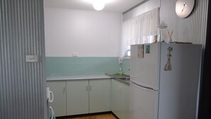 Una cucina con mobili chiari, un frigorifero e una sveglia appesa al muro.