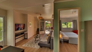 A modern living room with a sofa, a dining table, and a TV. There is a balcony with a view of greenery. - Apartment with terrace overlooking the park (Clohars Fouesnant)
