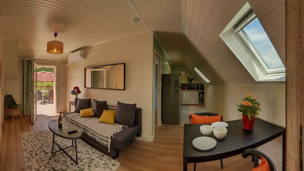 A spacious living area with a sofa, coffee table, and a dining table with chairs. A kitchen is visible in the background, and there is a skylight above the dining area. - Apartment with terrace overlooking the park (Clohars Fouesnant)