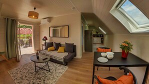 A spacious living area with a sofa, coffee table, and dining table. There is a skylight and a view of the outdoors. - Apartment with terrace overlooking the park (Clohars Fouesnant)