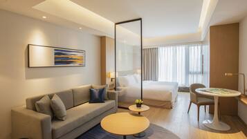 Ein modernes Hotelzimmer mit einer Couch, einem runden Couchtisch, einem Bett, einem Schreibtisch und einem großen Spiegel.