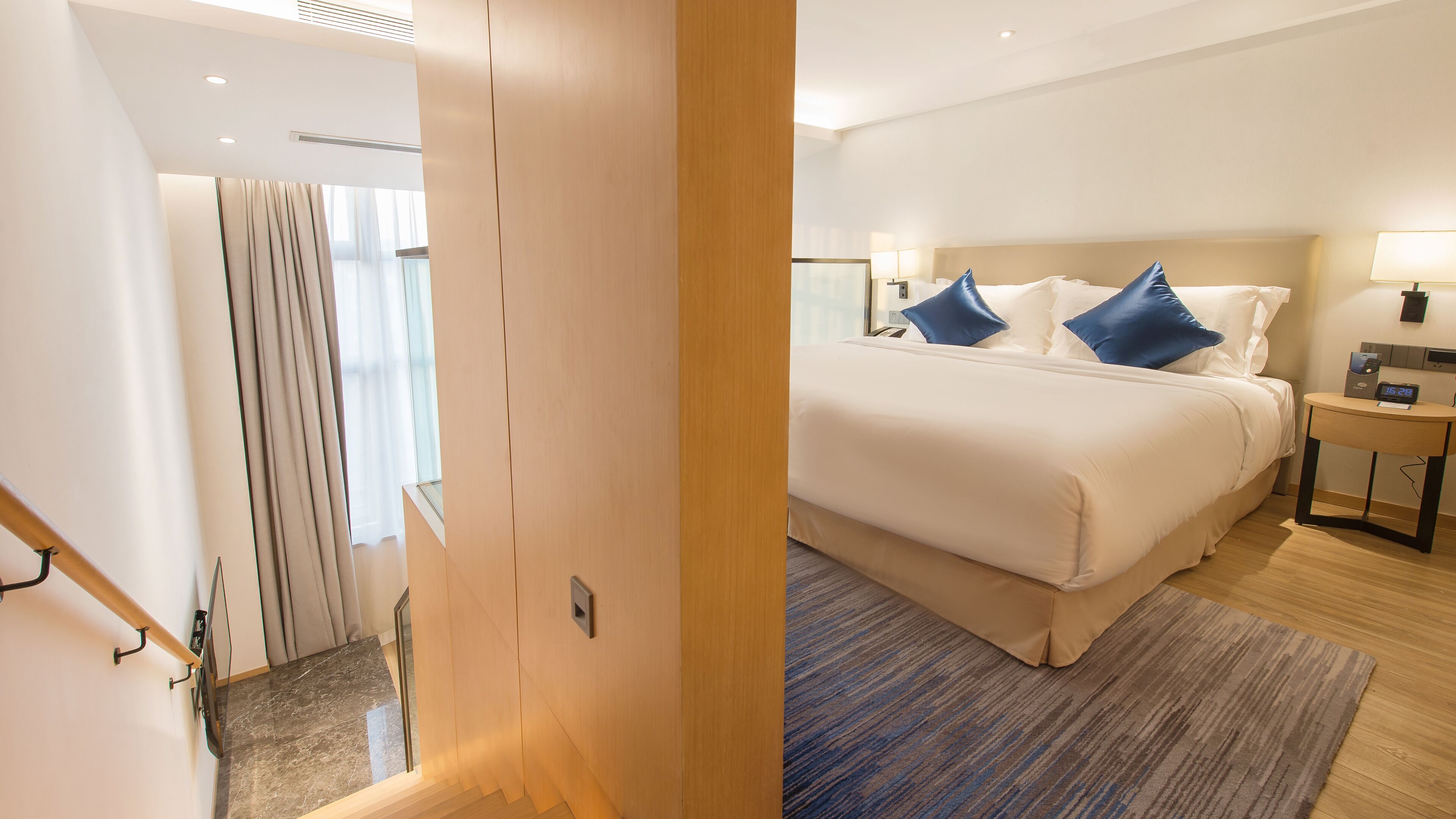 A hotel room with a bed, bedside table, and a view of the hallway.