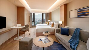 A hotel room with a bed, a sofa, a coffee table, a TV, and a city view.