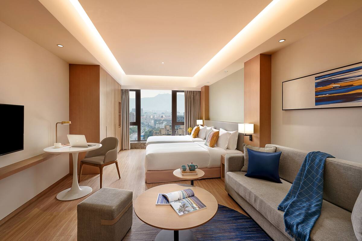 Une chambre d’hôtel avec un lit, un canapé, une table basse, une télévision et une vue sur la ville.