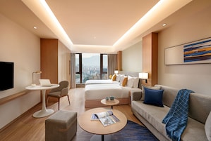 Una habitación de hotel con cama, sofá, mesa de centro, televisor y vistas a la ciudad.