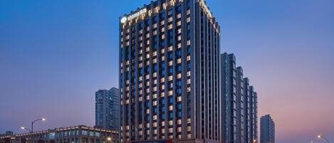 A high-rise building with illuminated windows and a sign for Shimao Hotel.