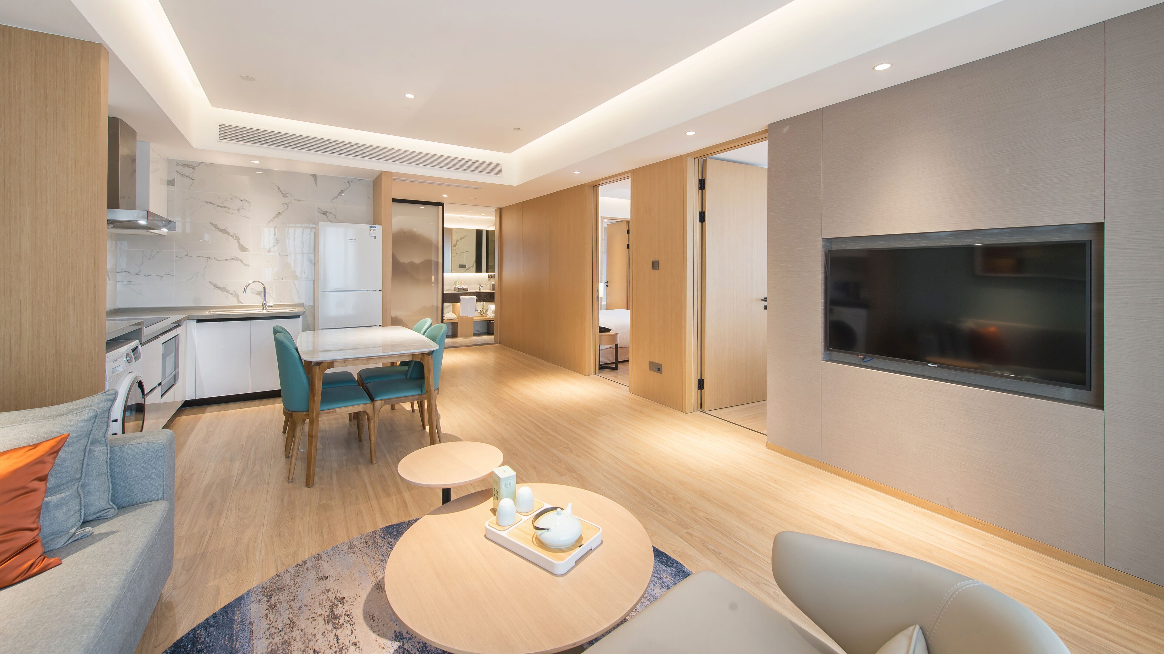 Et moderne hotelværelse med et tekøkken, et spisebord og et fjernsyn ophængt på væggen.