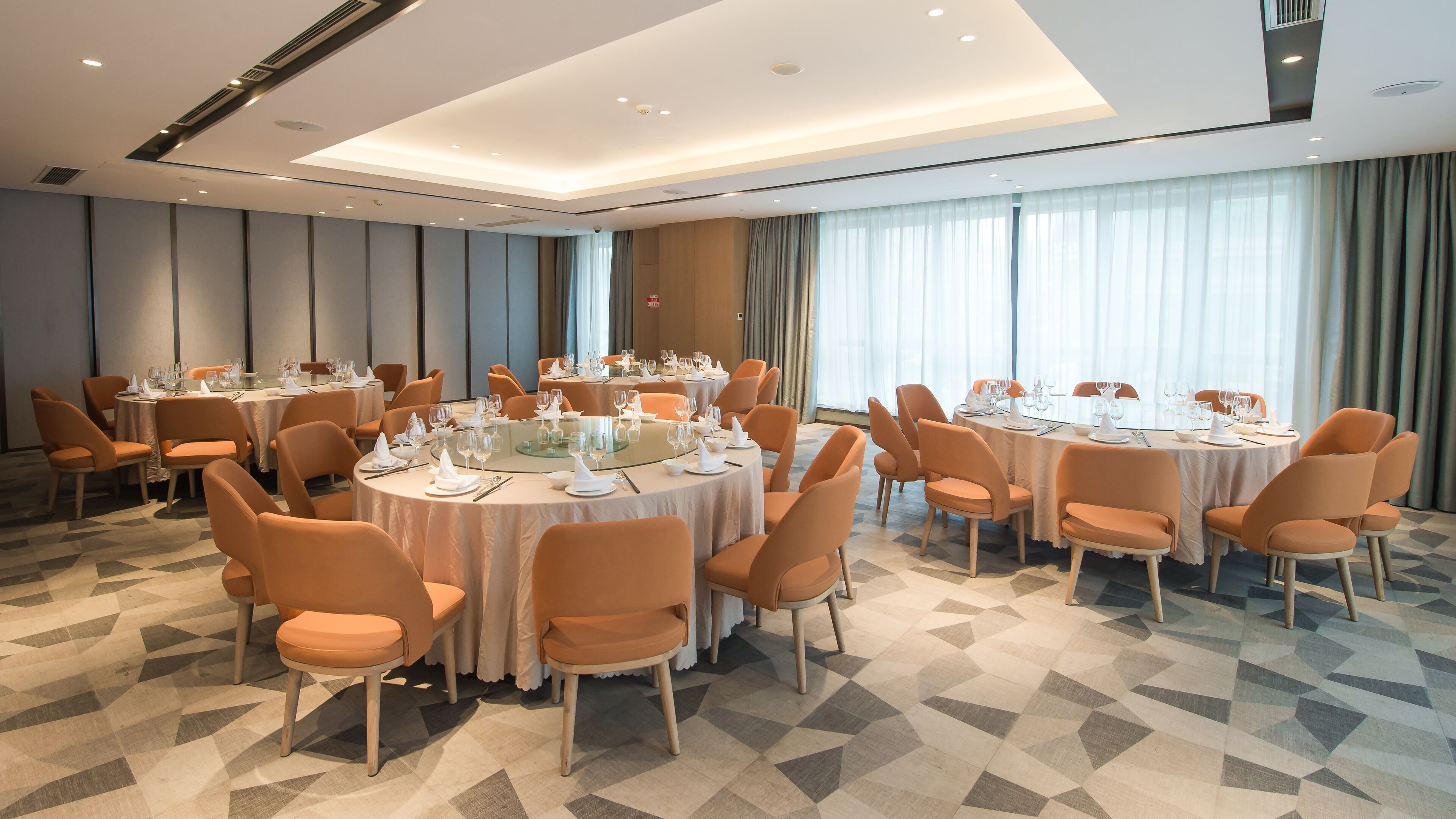 Un salón de conferencias con mesas redondas, sillas naranjas y un suelo con estampado geométrico.
