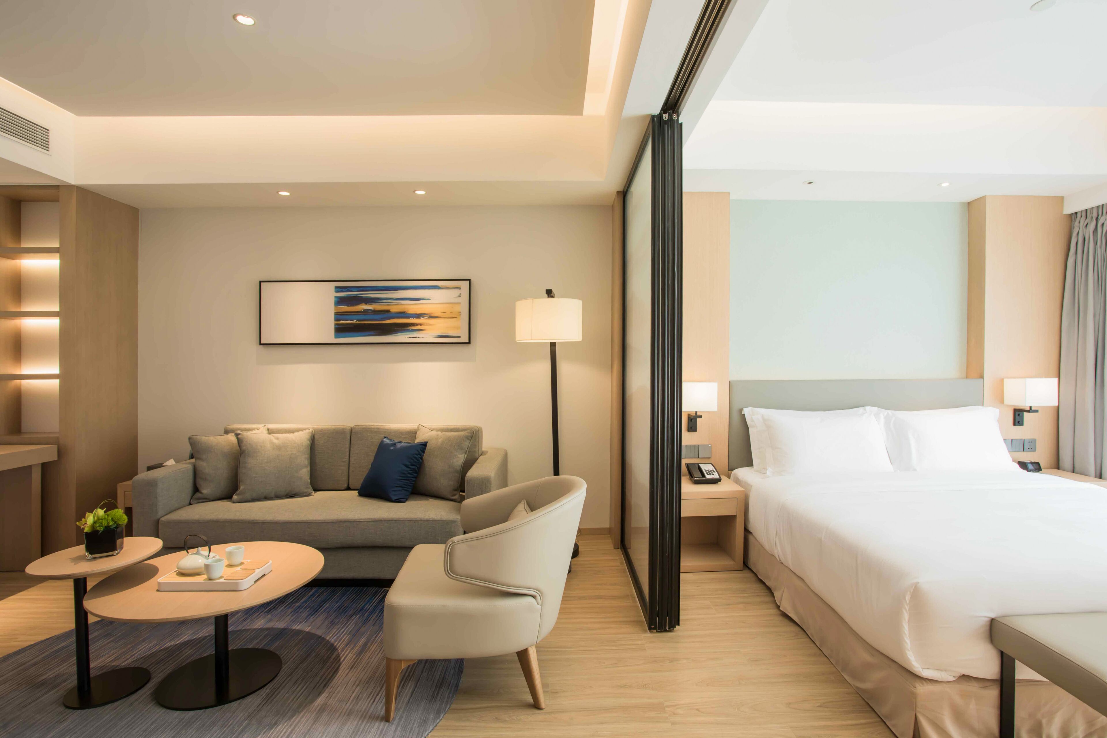 Une chambre d’hôtel moderne avec un lit, un canapé, une petite table et une lampe.