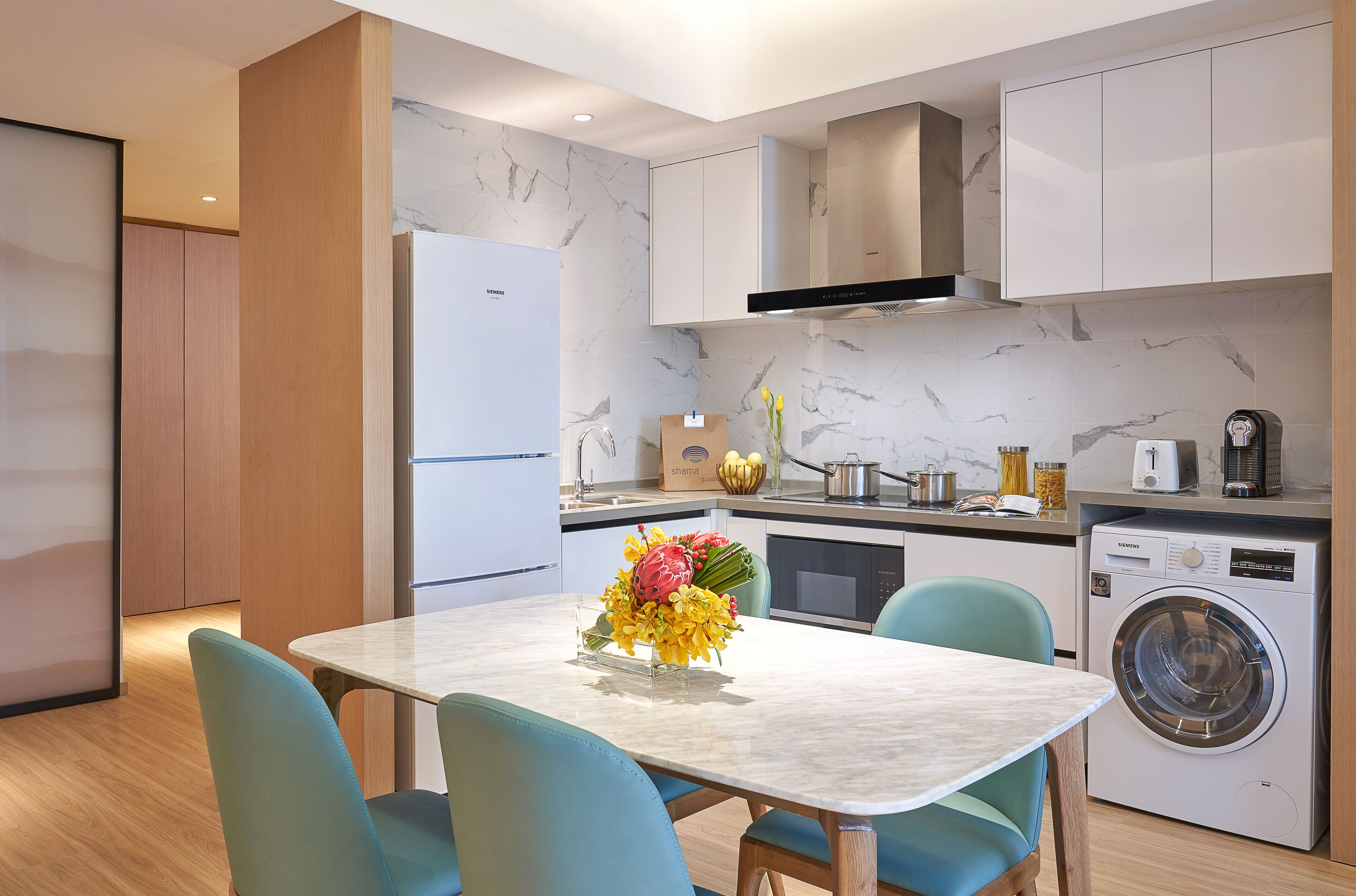 A modern kitchen with a marble backsplash, white cabinets, a built-in washing machine, and a dining table with chairs.