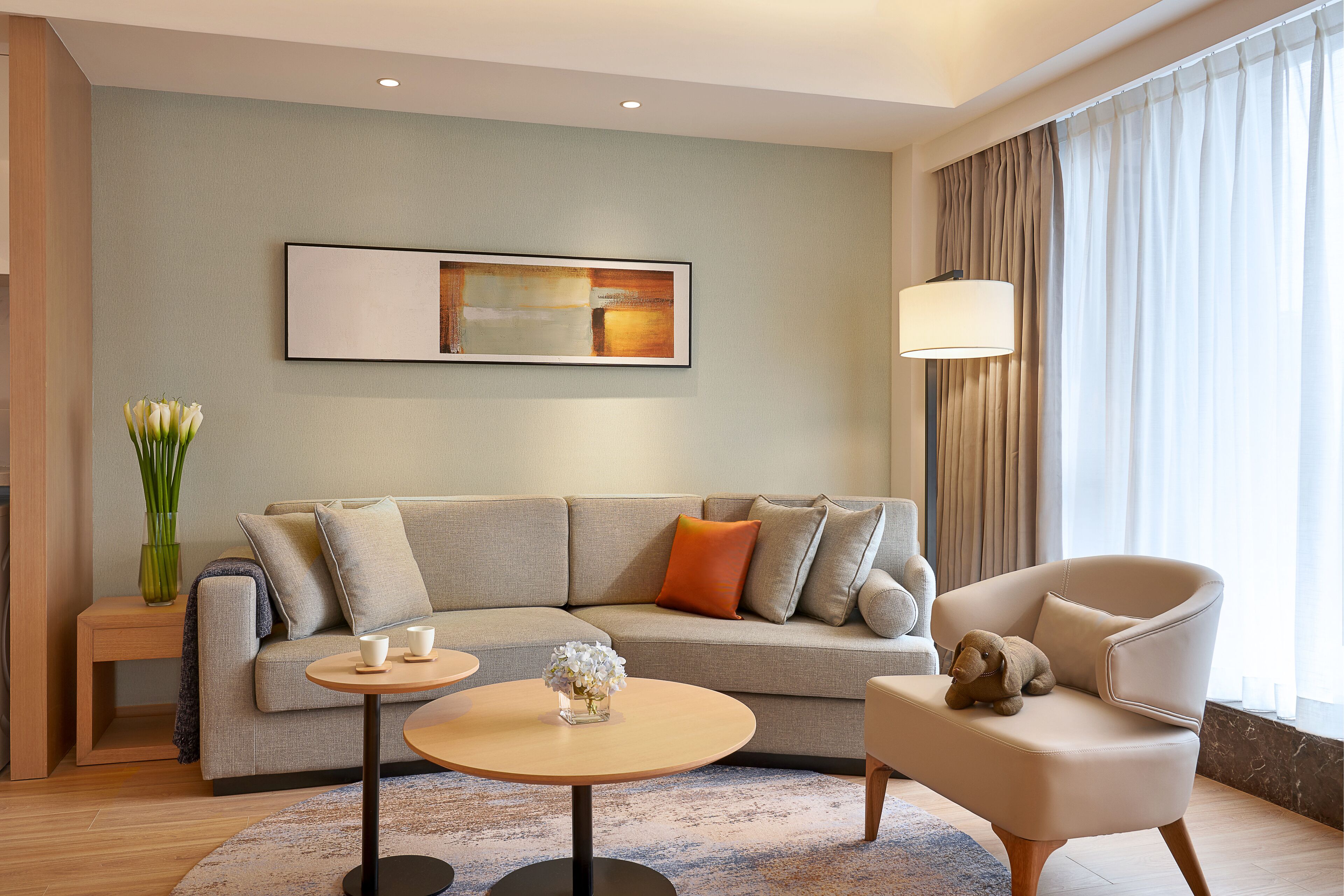 A modern living room with a sofa, armchair, coffee table, and a painting on the wall.