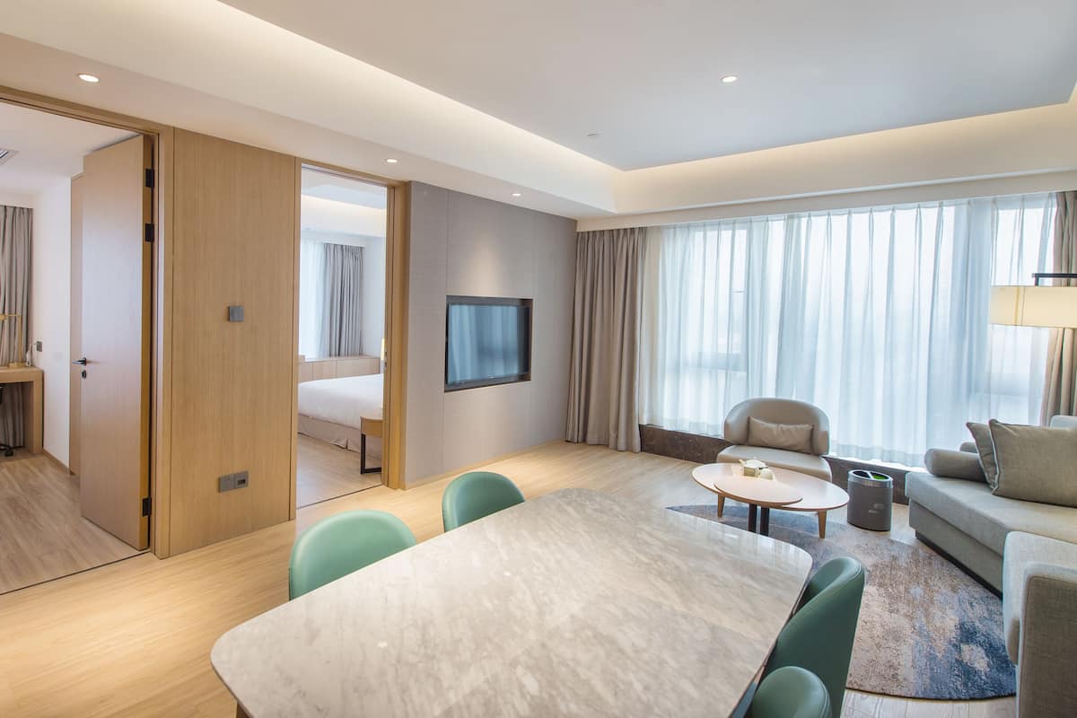 Une chambre d’hôtel moderne dotée d’un grand lit, d’un bureau avec une chaise, d’une table à manger avec des chaises, d’un canapé et d’un téléviseur fixé au mur.