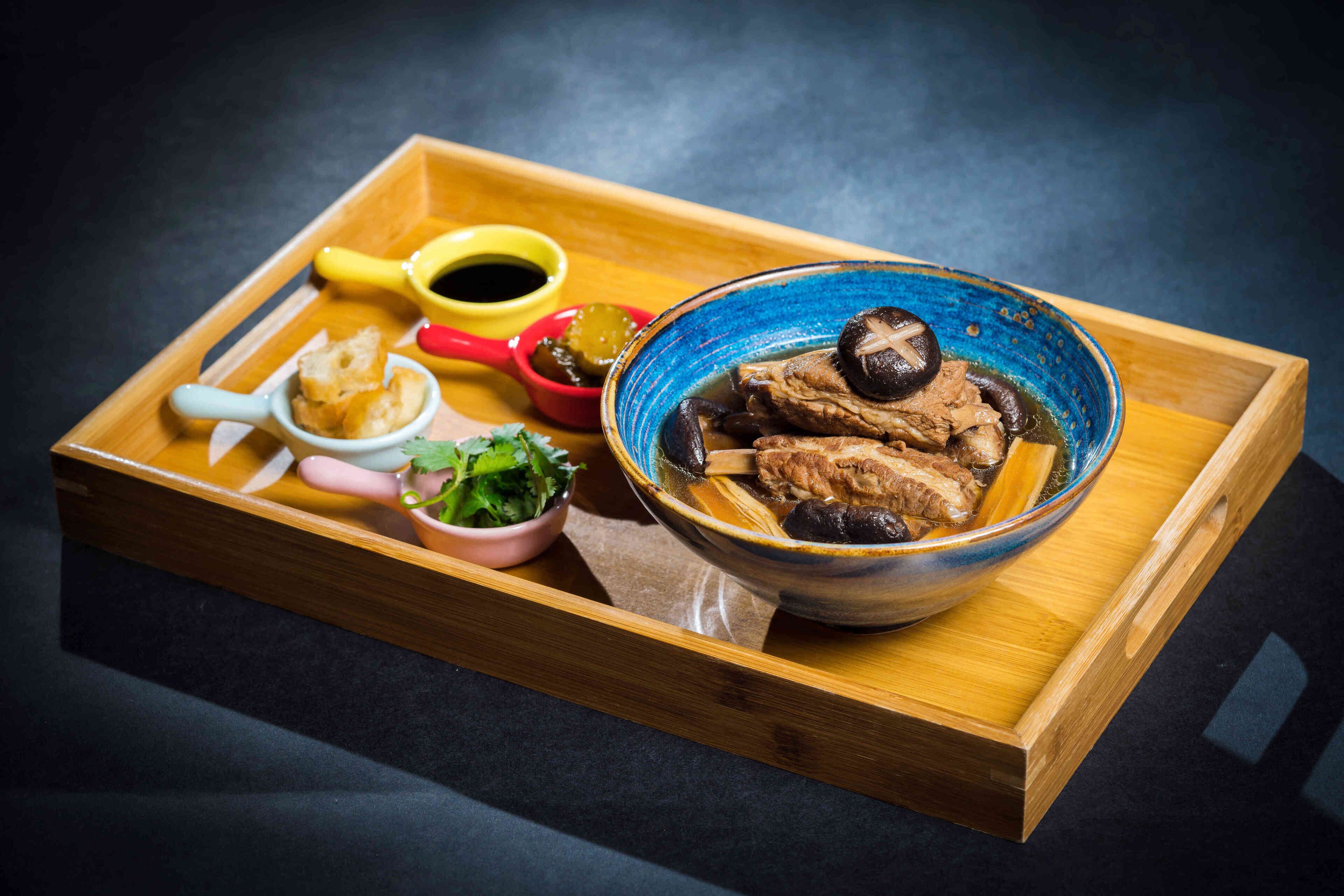 A wooden tray with a bowl of soup, a small bowl of greens, and a red cup.