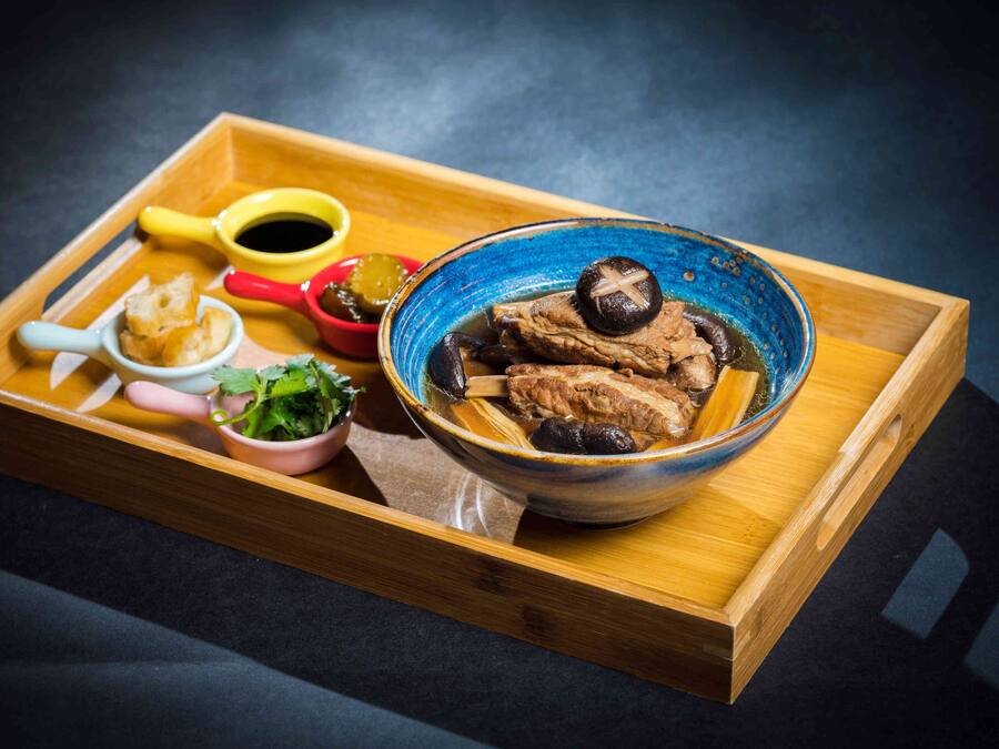 Una bandeja de madera con un tazón de sopa, un recipiente pequeño de vegetales verdes y una taza roja.