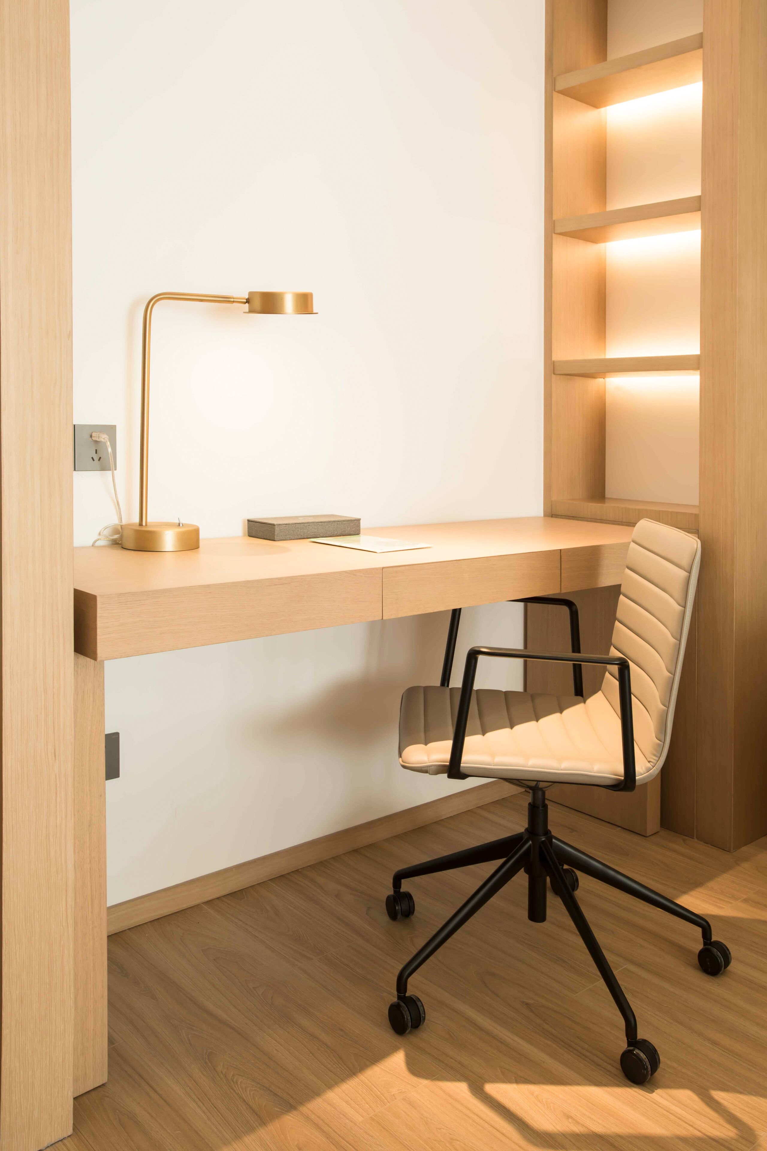 A modern workspace with a wooden desk, a black office chair, and a gold desk lamp.