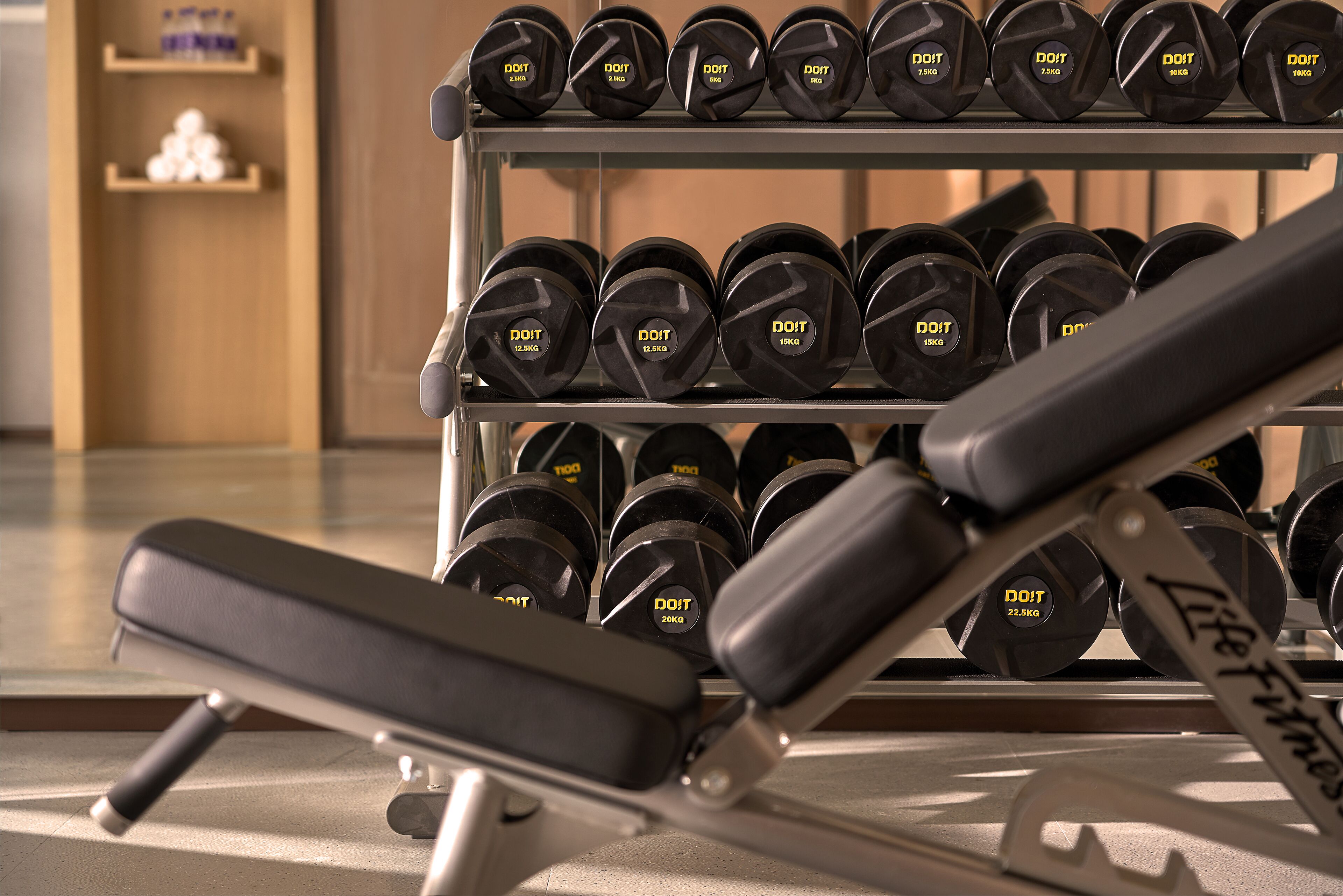Un gimnasio con una prensa de banca y un estante con mancuernas.