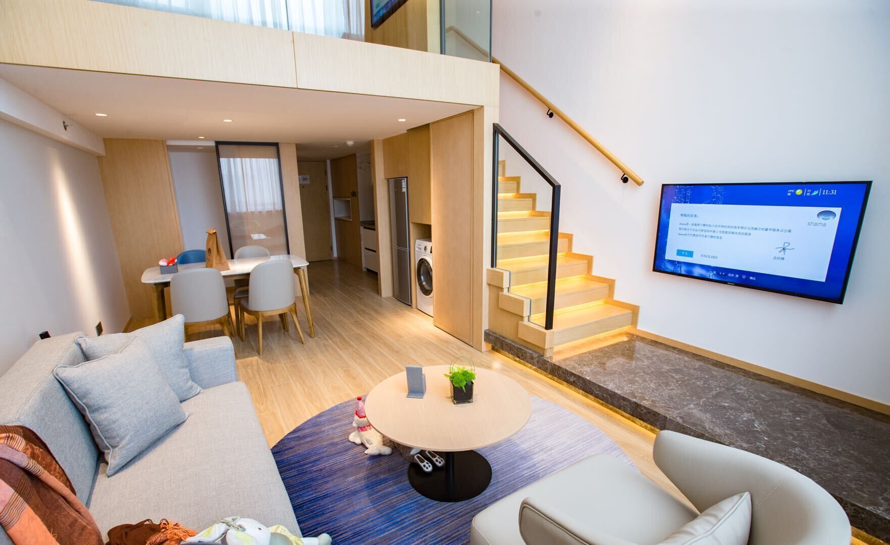 A modern hotel room with a living area, dining space, and a staircase.
