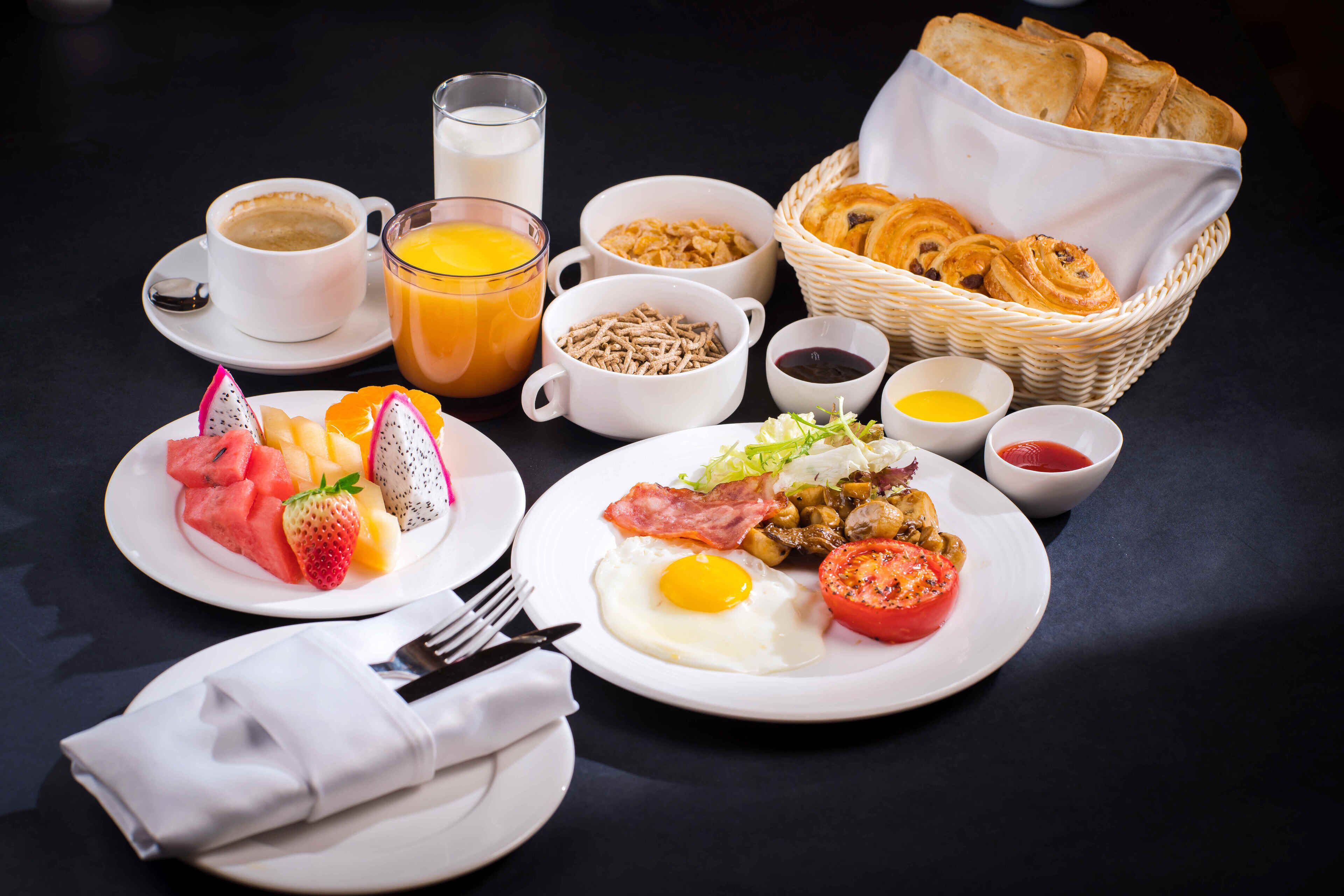A breakfast setting with plates of food, a basket of bread, and a cup of coffee.