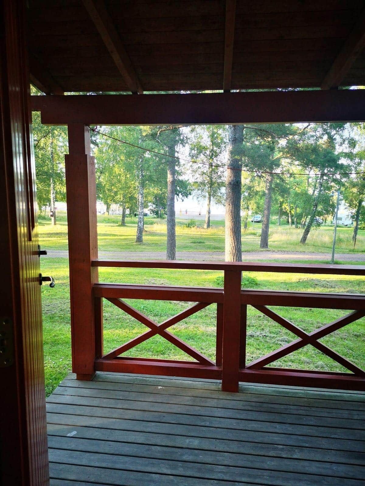 A wooden deck with a railing, leading to a grassy area with trees.
