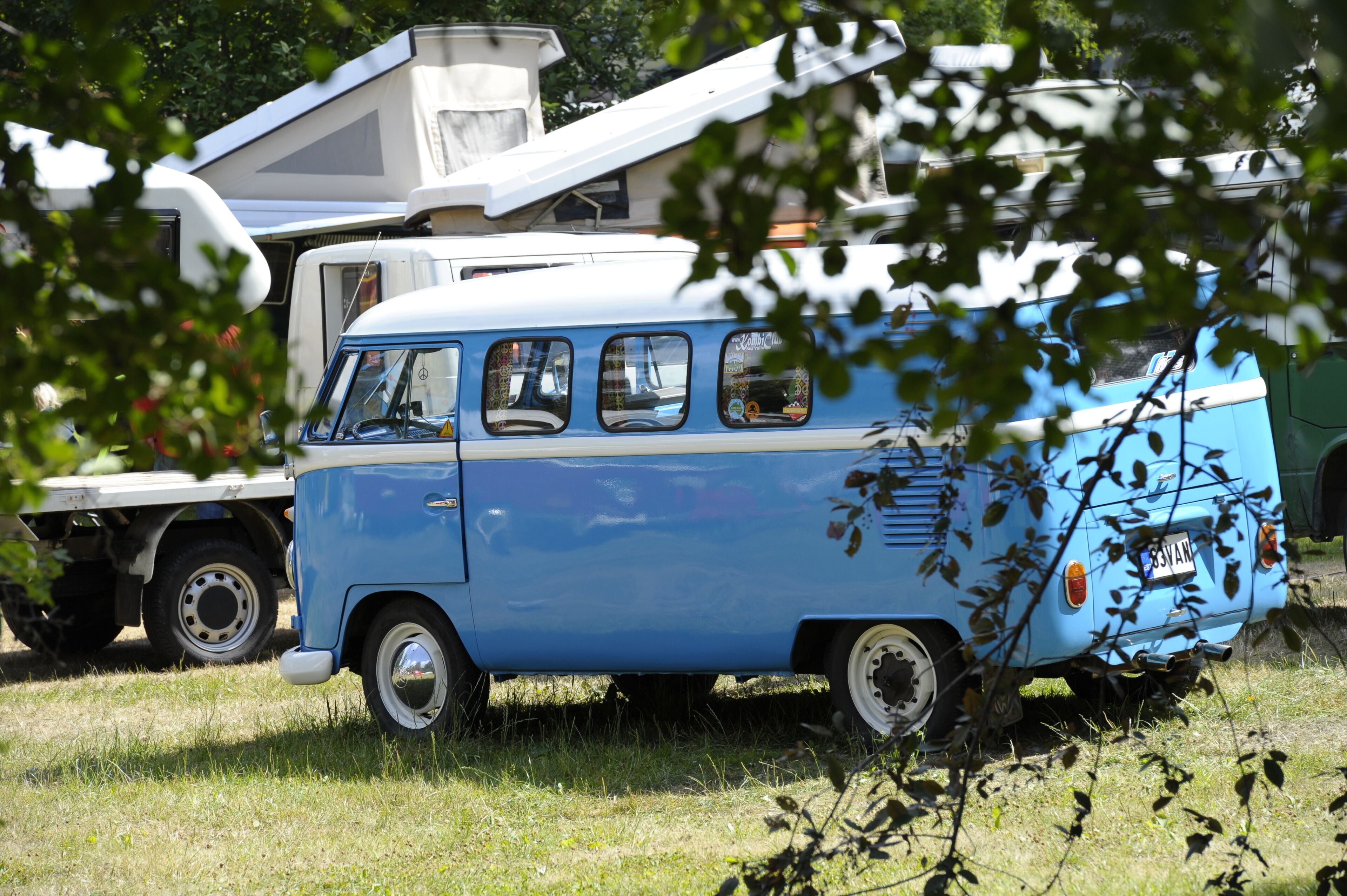 A blue and white camper van parked in a grassy area with a trailer attached.