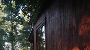 A wooden cabin with a large window, surrounded by trees and a grassy area. - Gröna Uddens Camping (Mariehamn)