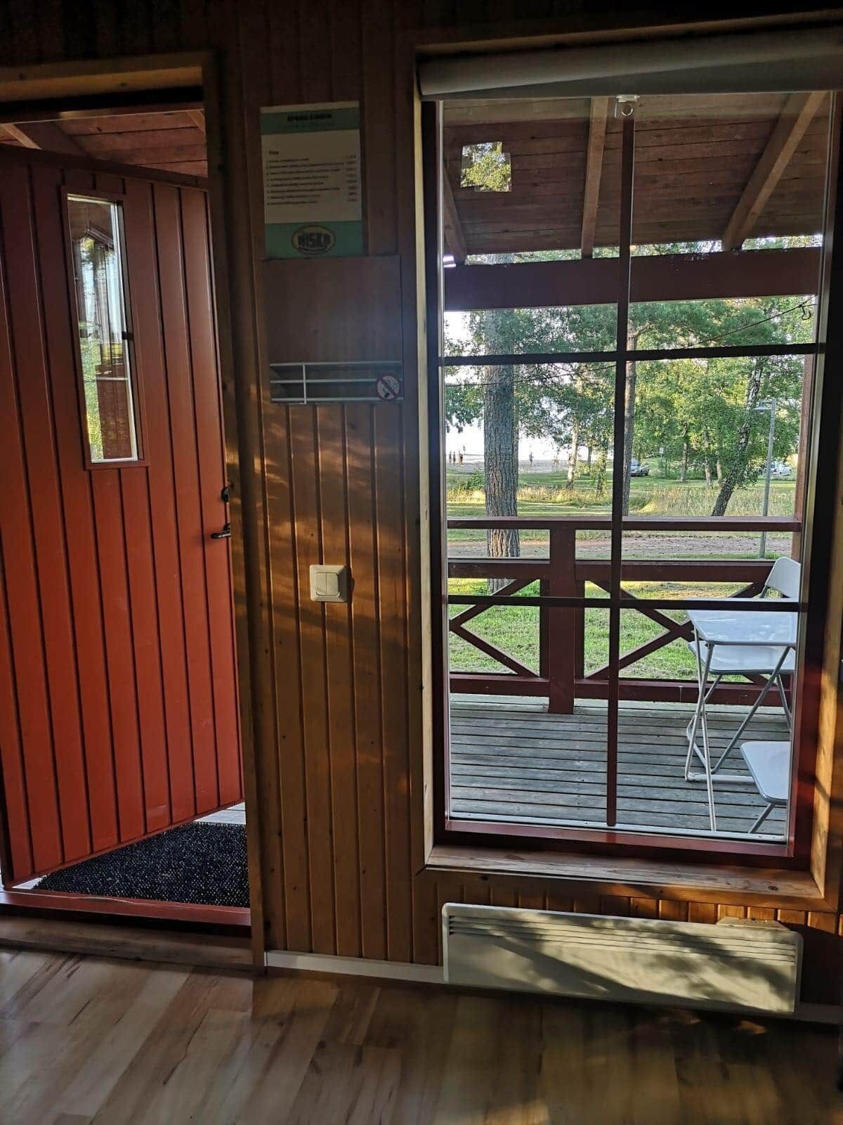 A wooden room with a large window, a door, and a small table with chairs outside.