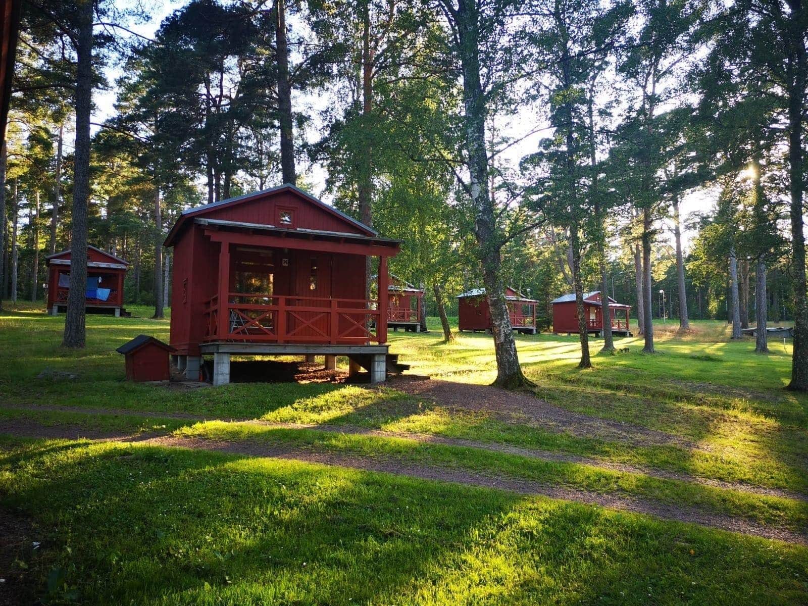 Punaisia mökkejä rivissä metsäisellä alueella, jonka halki kulkee ruohopäällysteisiä polkuja.