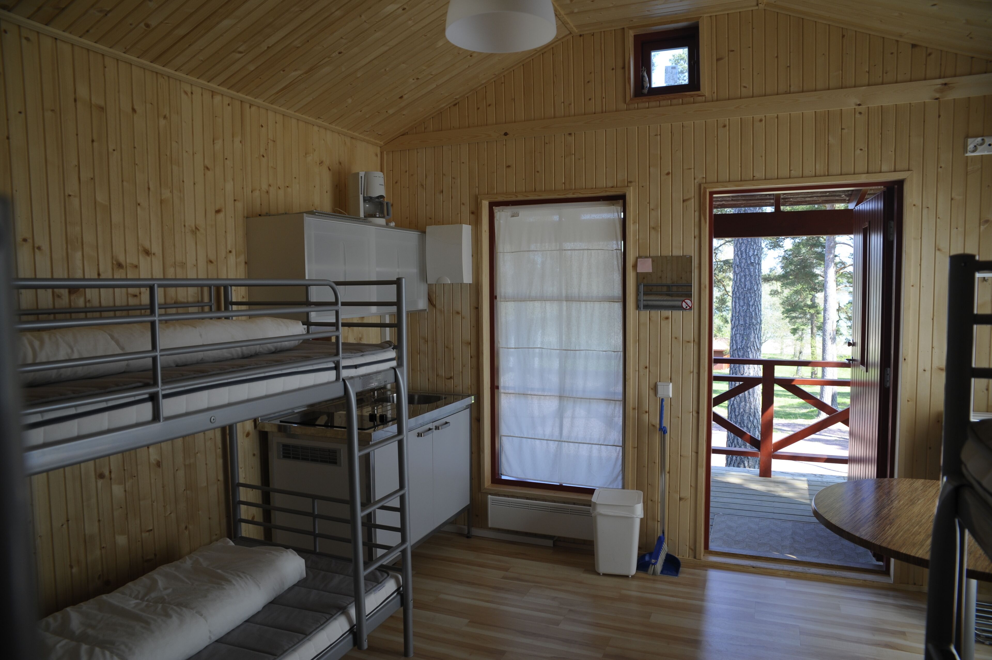 A wooden cabin with bunk beds, a kitchenette, and a door leading outside.