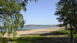 A beach with a clear view of the water, a sandy shore, and a distant hill. - Gröna Uddens Camping (Mariehamn)