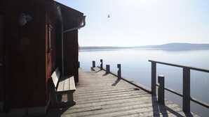 A wooden pier leading to a calm body of water, with a wooden building on the left and a clear sky above. - Gröna Uddens Camping (Mariehamn)