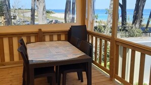 A covered outdoor deck with a wooden table and chairs, overlooking a beach and ocean view. - Rendezvous with the Sea - Mobilhome Vue Mer Conguel 4* (Conguel sea view mobile home) (Quiberon)