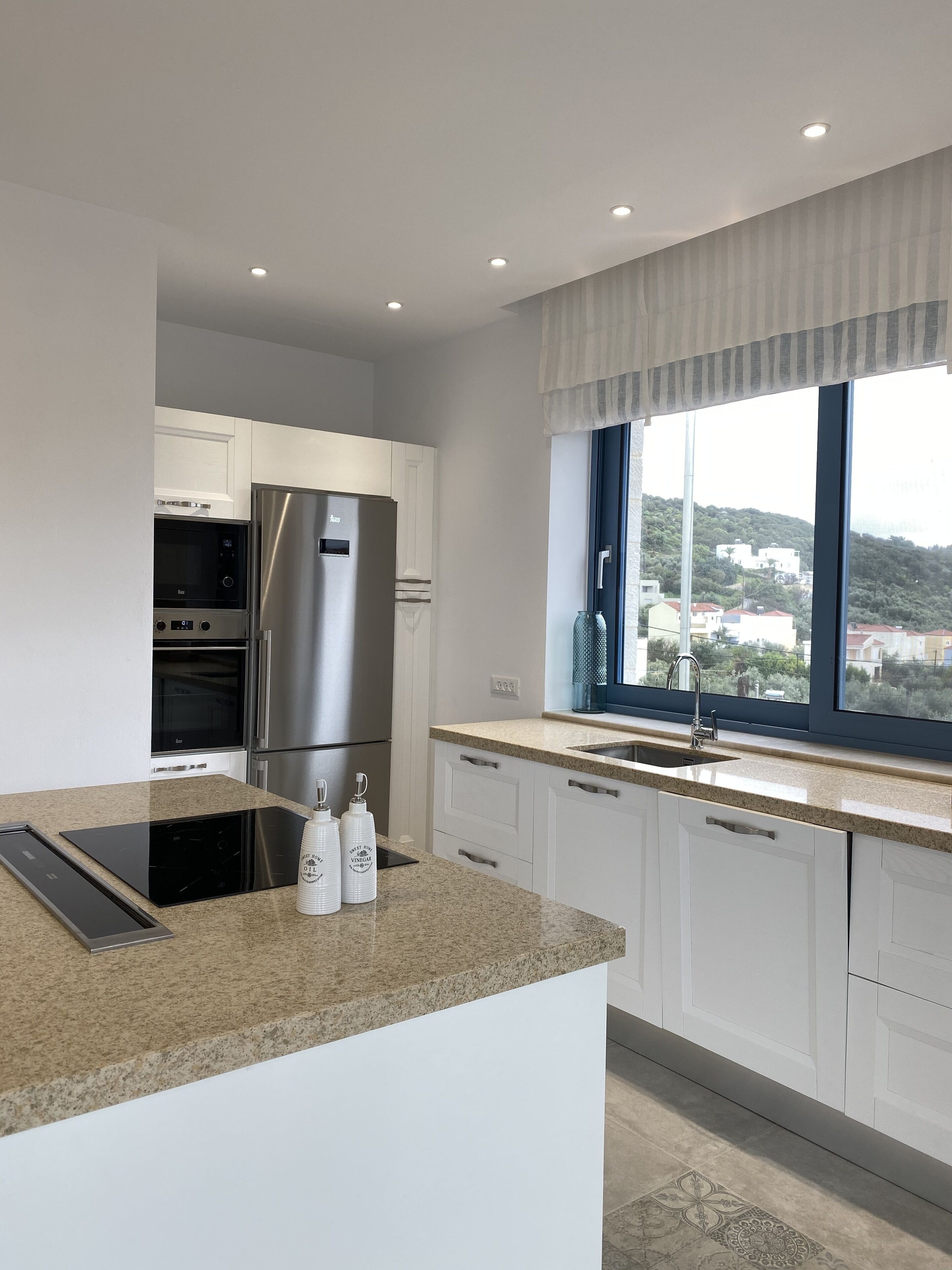 A modern kitchen with stainless steel appliances, a granite countertop, and a window with a view of a hillside.